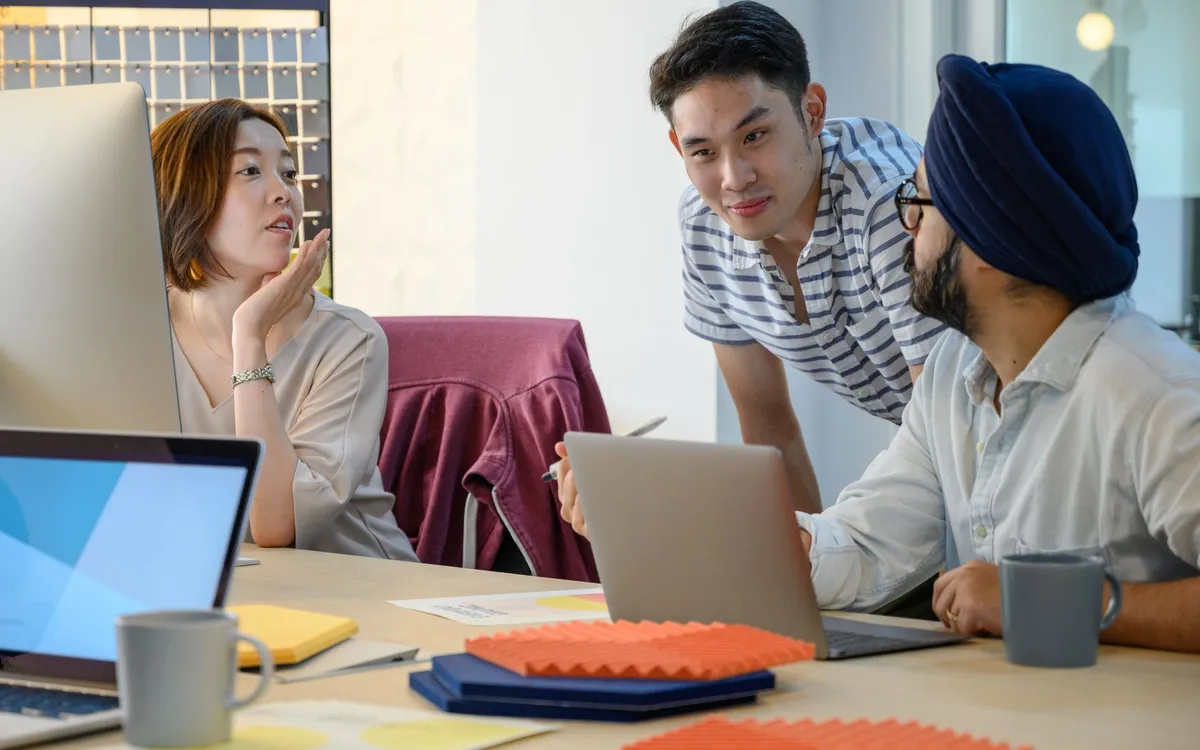 Three people discussing work together around laptops
