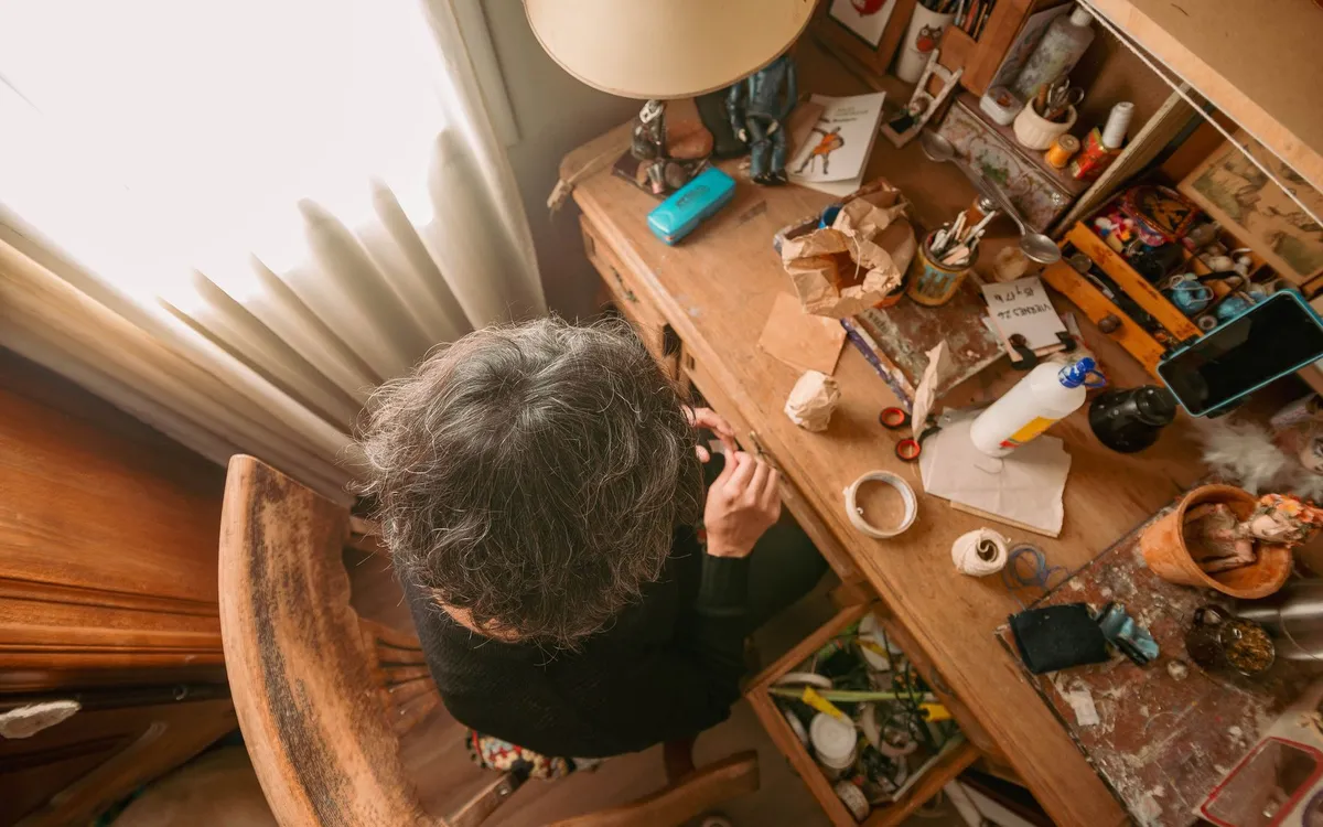 An overhead view of an artist working at a busy wooden desk